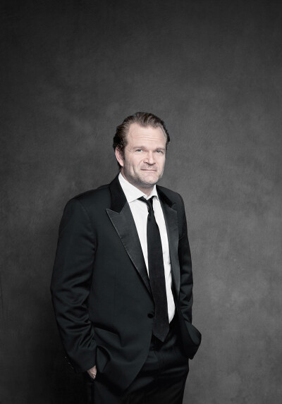 Sebastian Knauer Musiker - steht im schwarzen Smoking vor Wand und lächelt beide Hände in den Hosentaschen Farbfotografie - 2012 Foto Peter Koehn