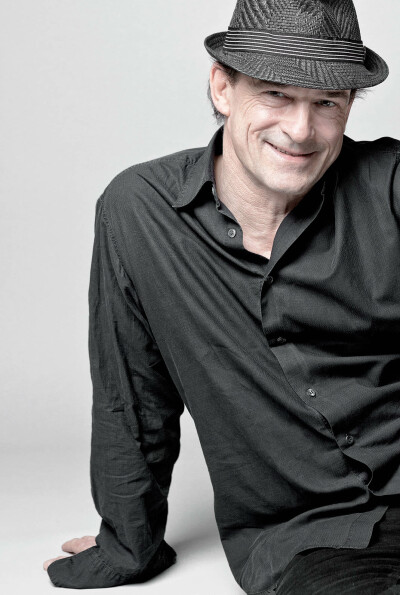 Thomas Sarbacher Schauspieler - schwarzes Hemd Hut sitzt auf dem Boden lacht Farbfotografiebetreut von Agentur Velvet - 2012 Foto Peter Koehn